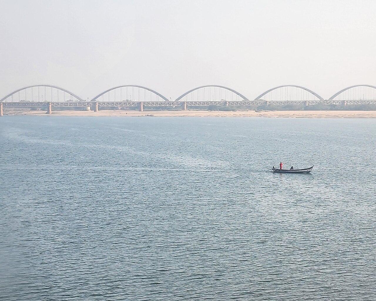 A boat on the wide Godavari river with the arch bridge at Rajahmundry behind